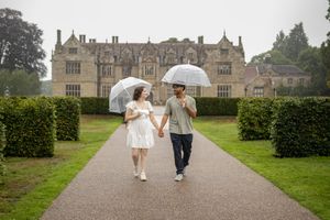A couple strolls along a grand historic estate's pathway under cloudy skies.