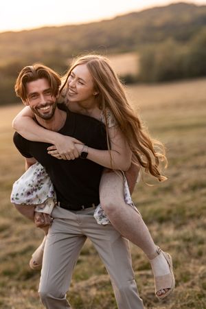 Playful couple laughing and spinning in a sunlit field at golden hour.