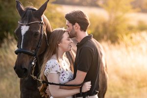Couple poses with their horse in a sun-drenched field during golden hour.