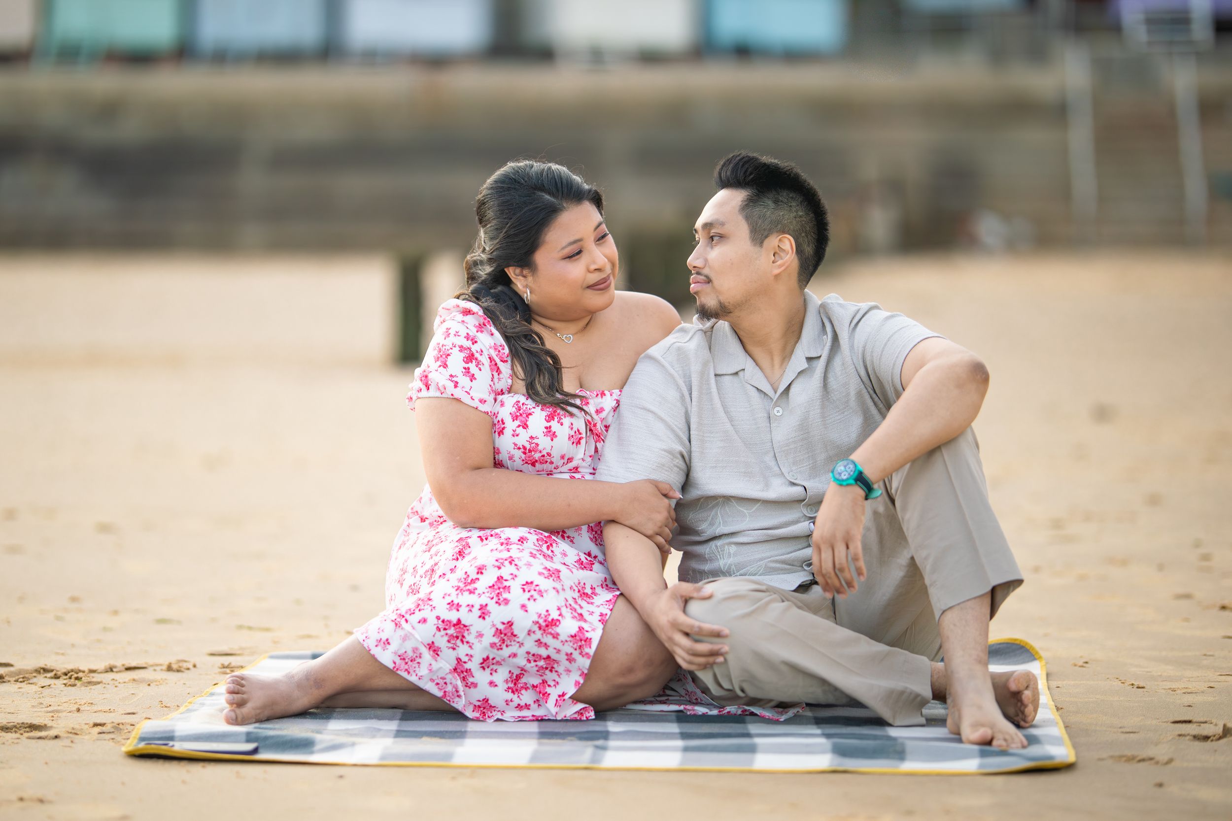 A couple sitting on a blanket at the beach having an intimate conversation.