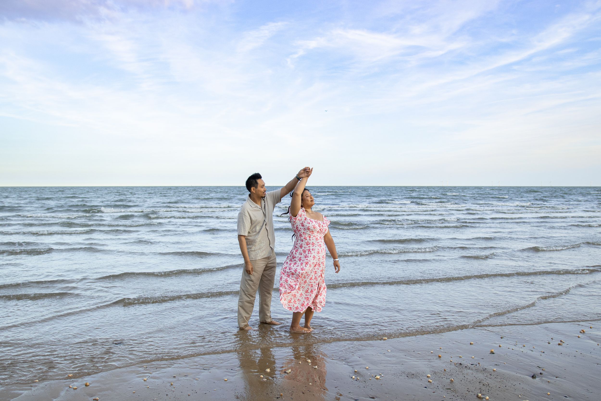 A couple dancing together on the beach with ocean waves in the background.