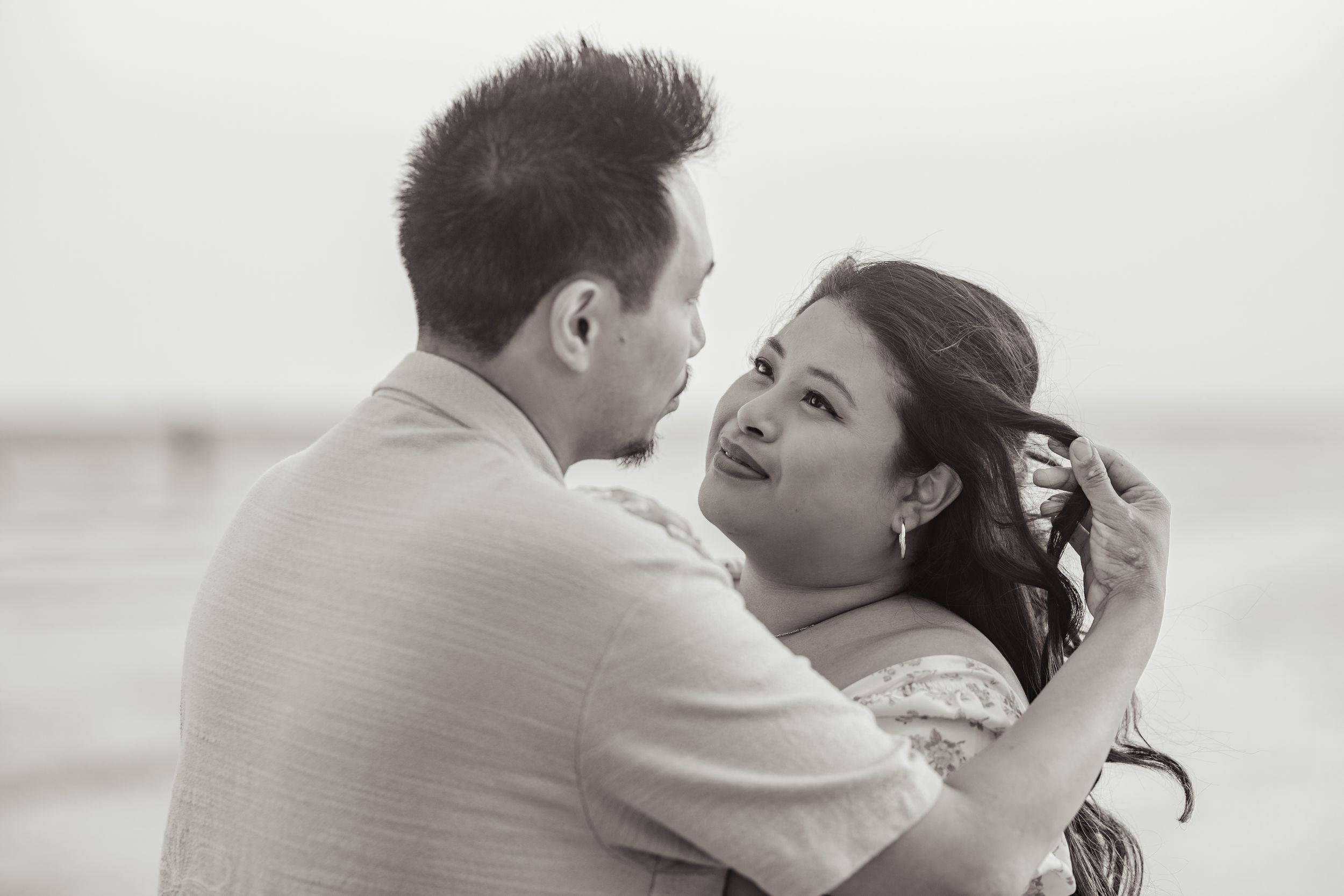 An intimate black and white portrait of a couple sharing a tender moment at the beach.