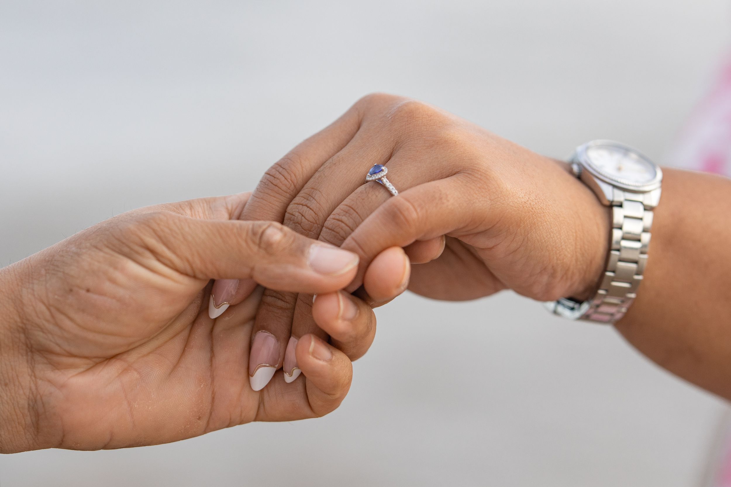 Close-up of hands exchanging rings with a silver watch in the background.