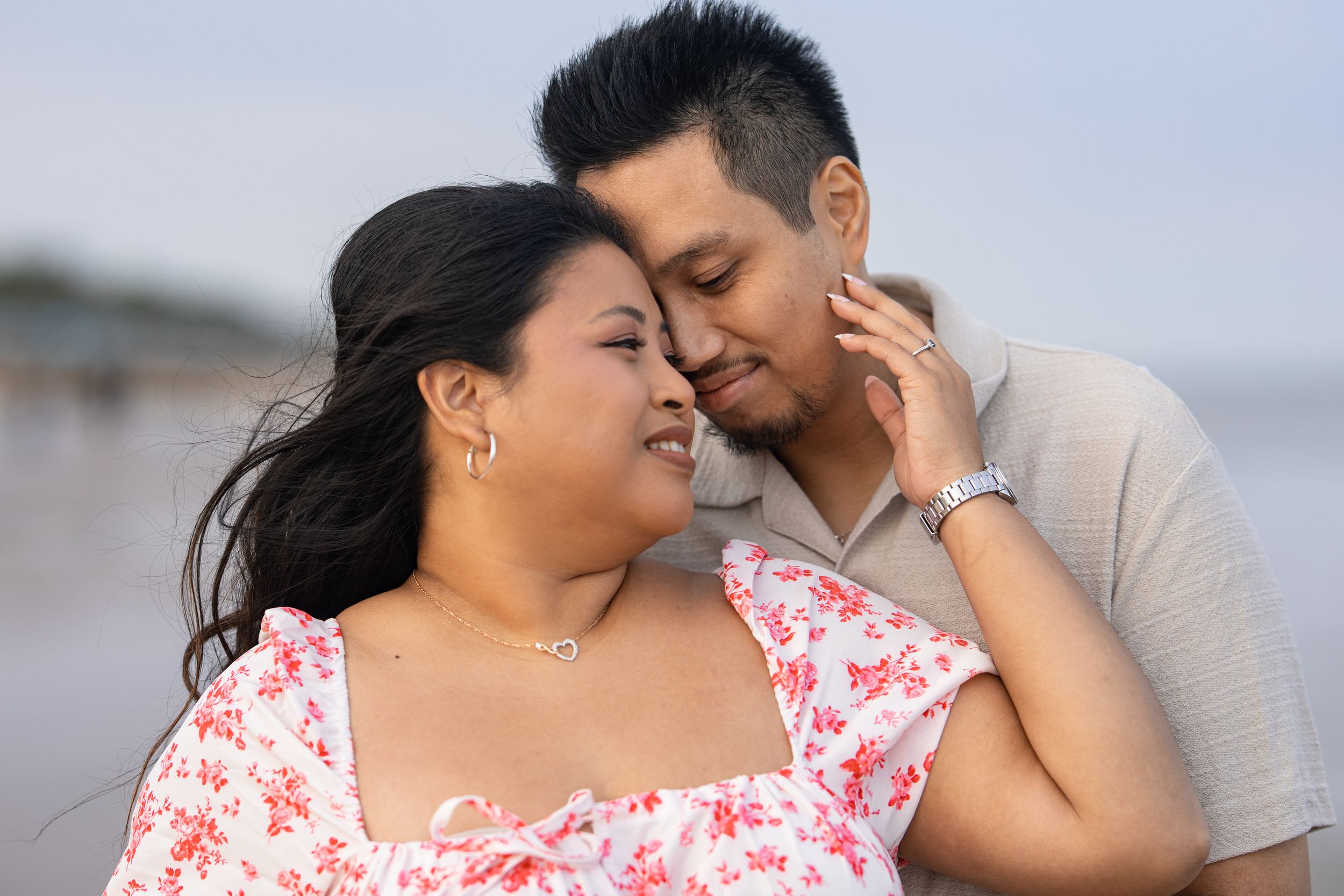 A romantic beach portrait of a couple in casual attire sharing a tender moment.