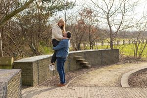 Couple sharing intimate moments along a curved stone path surrounded by bare winter trees.