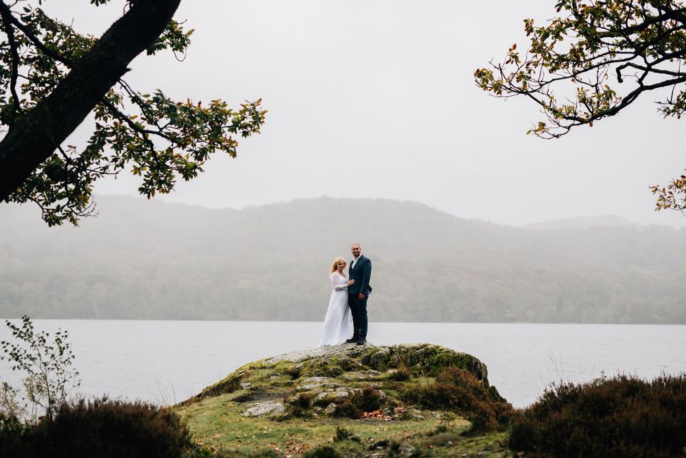 Couple embraces on a misty mountain overlook with dramatic coastal scenery in the background.