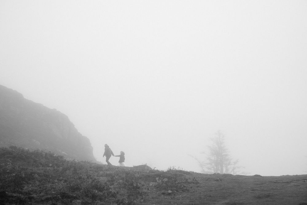 Two silhouetted figures walk along a misty mountain ridge with dramatic foggy atmosphere in the background.