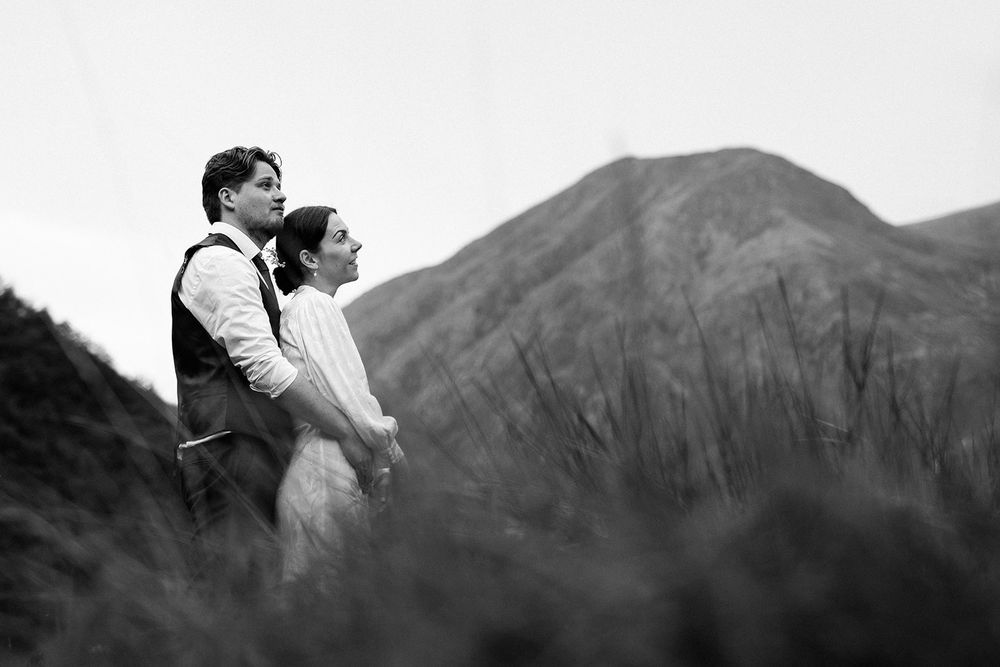 A couple shares a romantic kiss while hiking through misty mountains and green meadows.