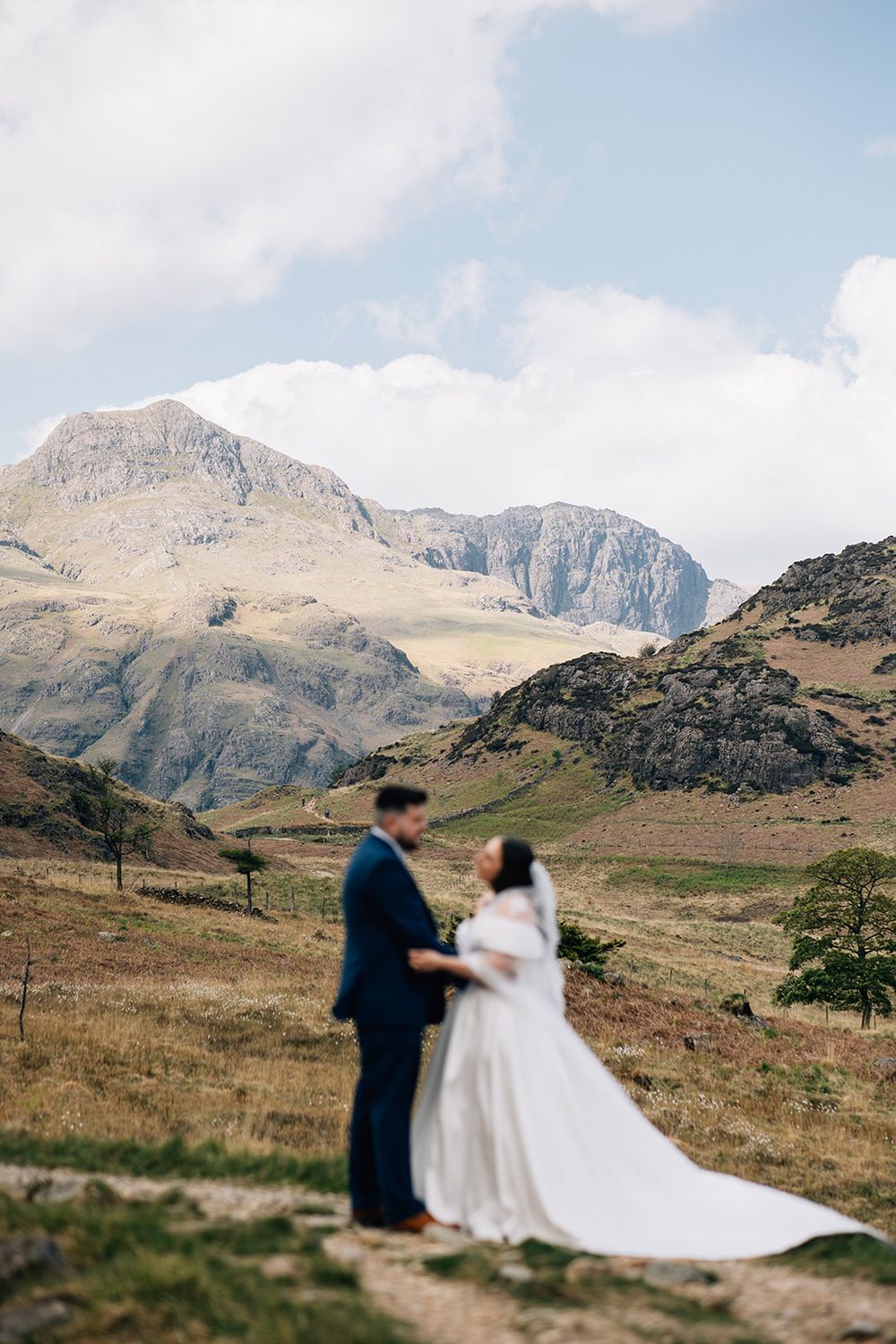 A romantic wedding couple stands against the dramatic backdrop of rugged mountain peaks in a scenic landscape.