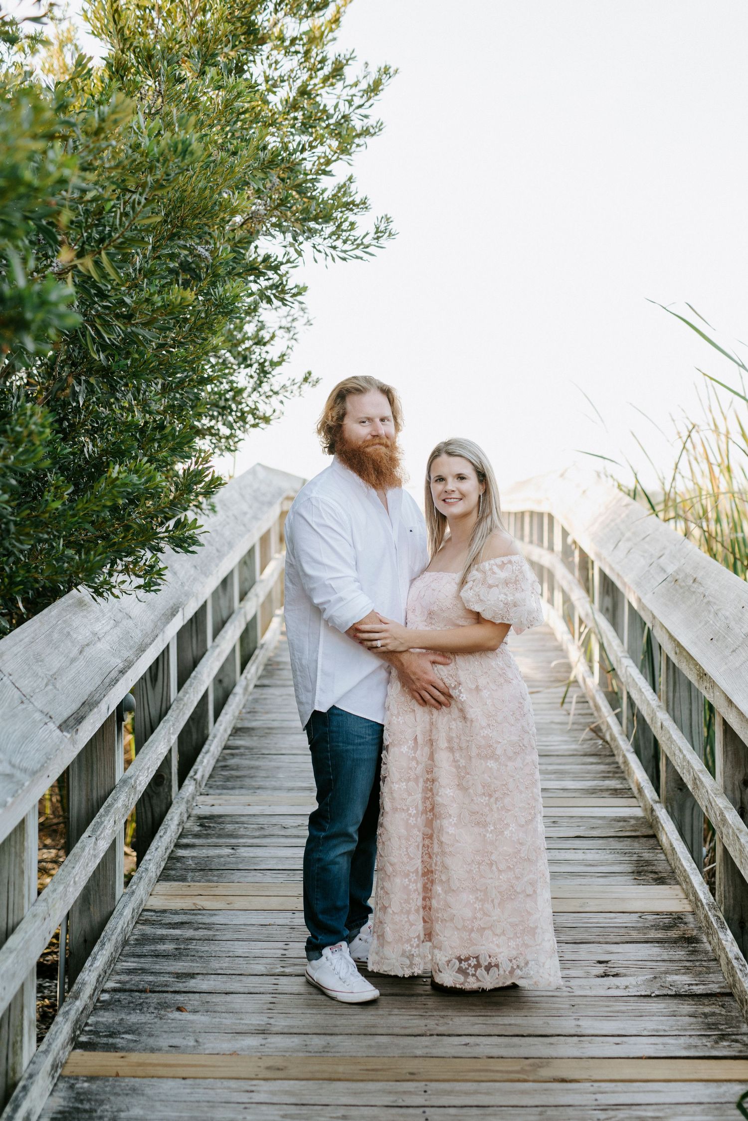 Couple in romantic poses on a wooden boardwalk surrounded by green foliage in an outdoor setting.