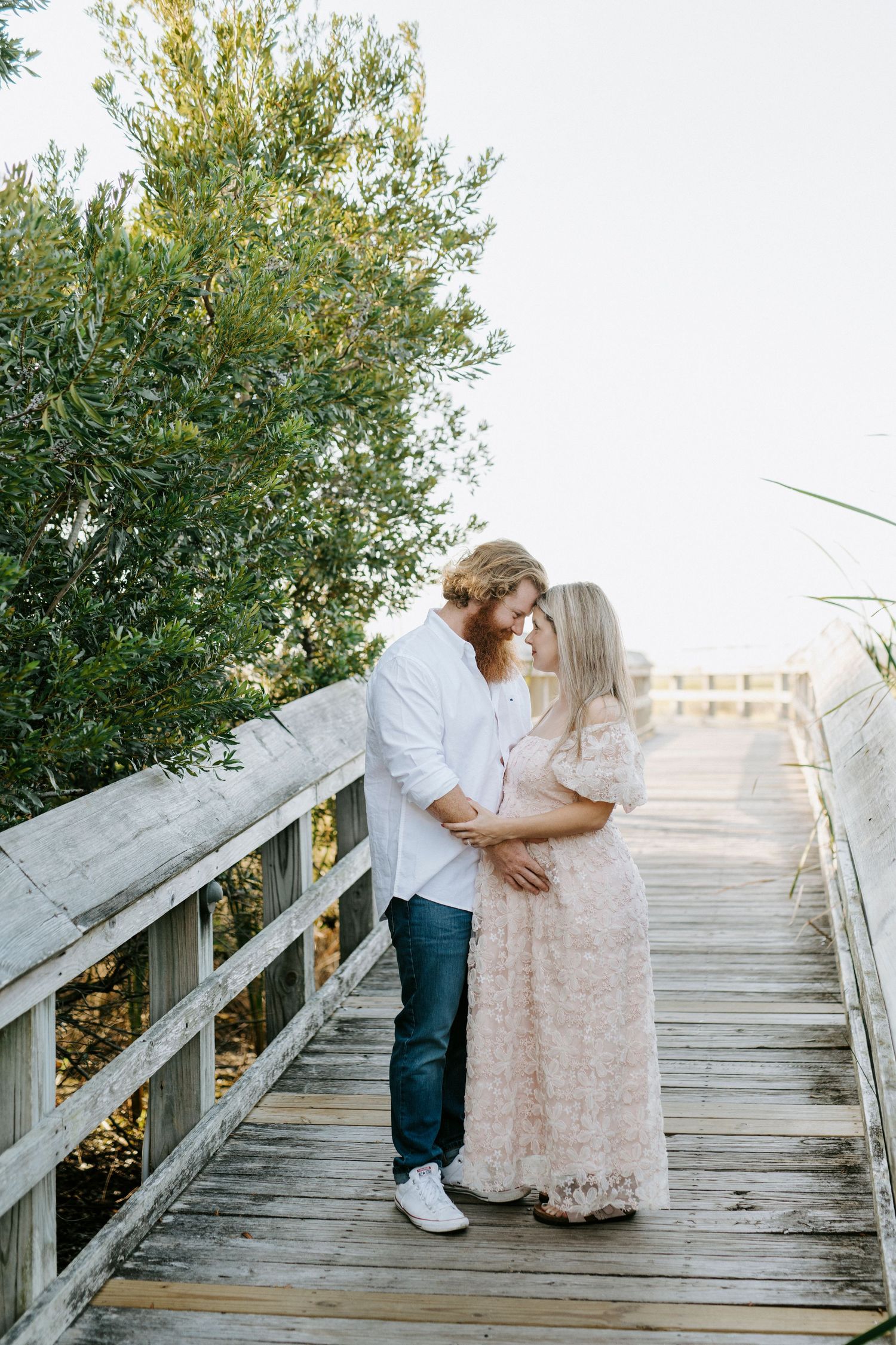 Romantic couple embraces on white wooden boardwalk stairs surrounded by lush green foliage at sunset.
