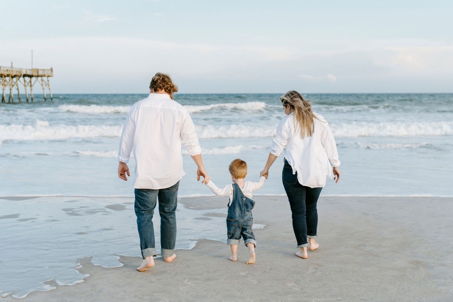 Family wearing blue and white outfits walking together on beach at sunset while holding hands.
