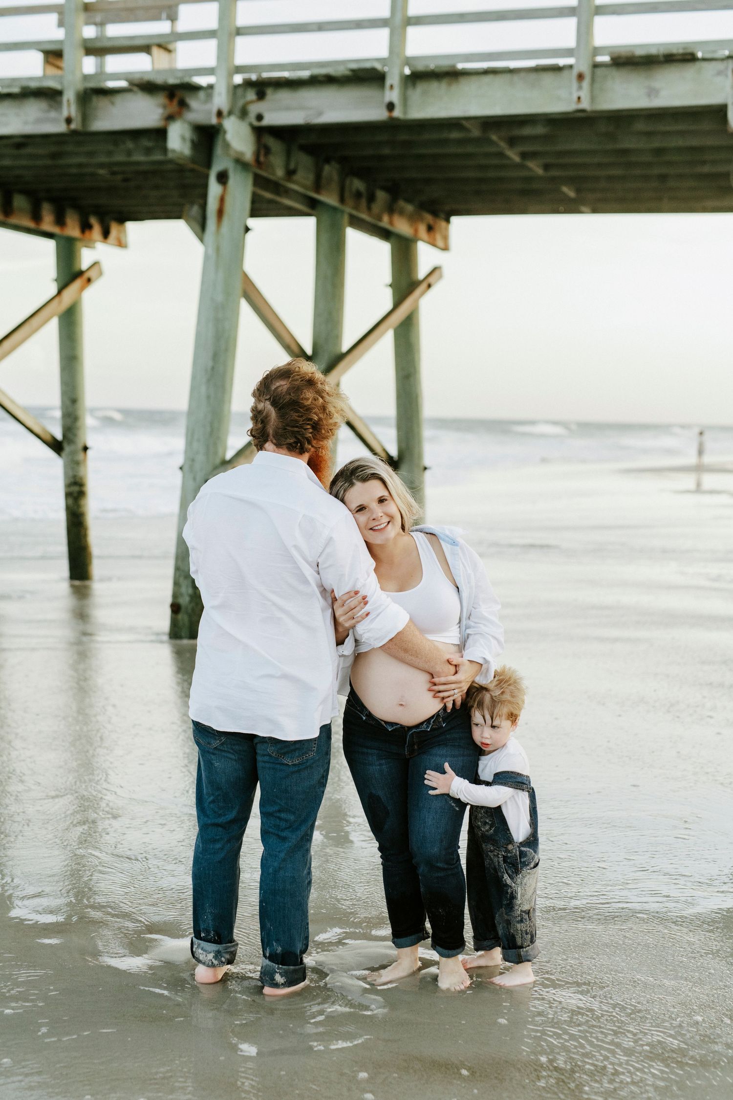 Three heartwarming photos show adults and a child playing together on a sandy beach beneath a wooden pier.