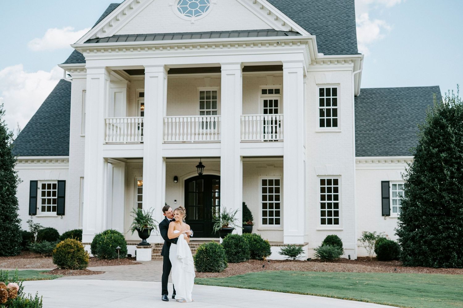 A luxurious white colonial mansion with Greek revival elements stands proudly against a cloudy sky.