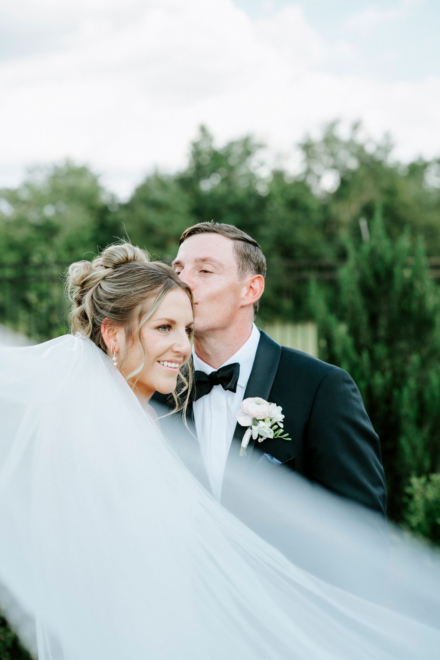 A romantic wedding portrait showing a flowing white veil against a natural green backdrop.
