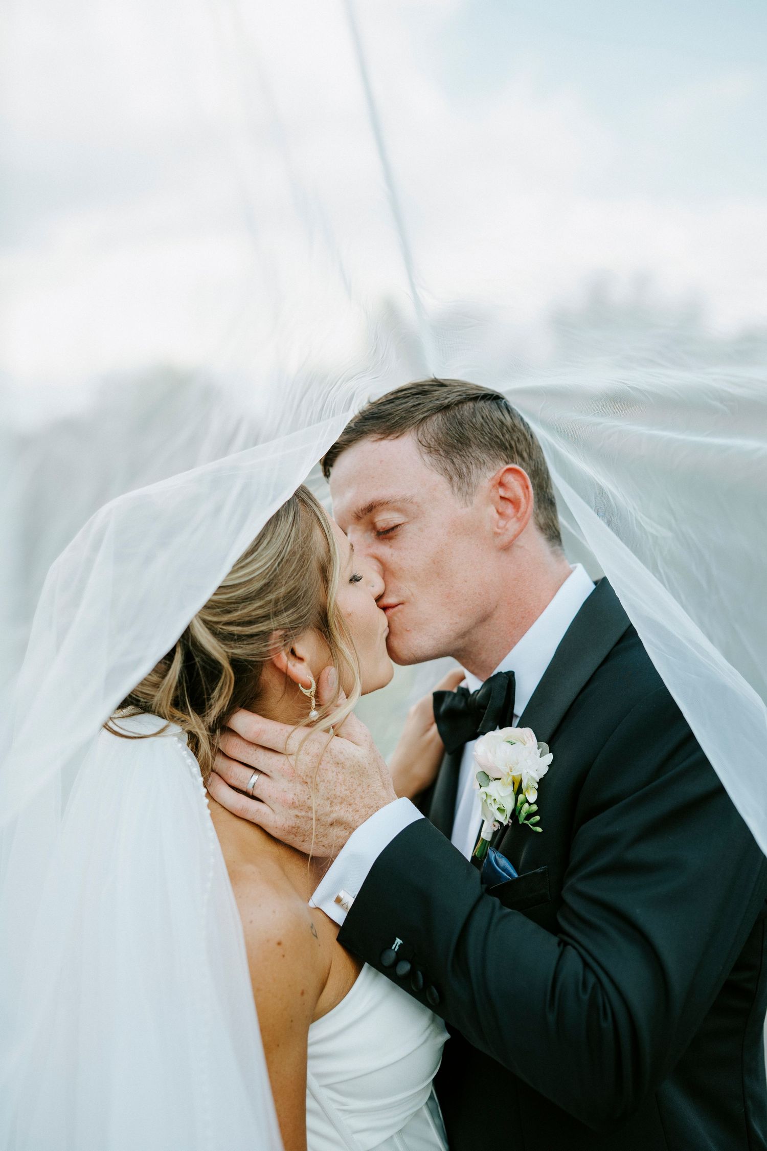 An intimate wedding moment captured under a flowing white veil with greenery in the background.
