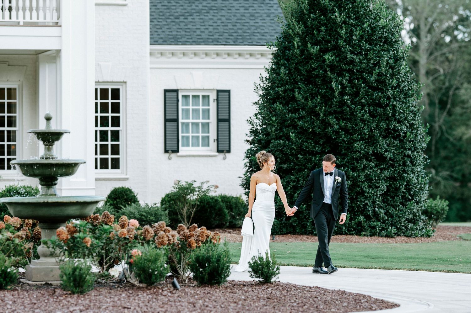 A wedding dress photoshoot in front of a grand white mansion with ornate landscaping and architecture.