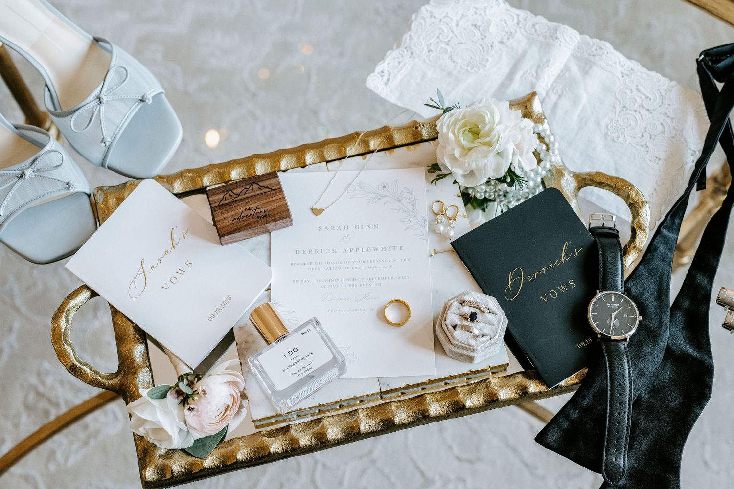 Wedding details flatlay with invitations, rings, shoes and flowers arranged on a gold tray.