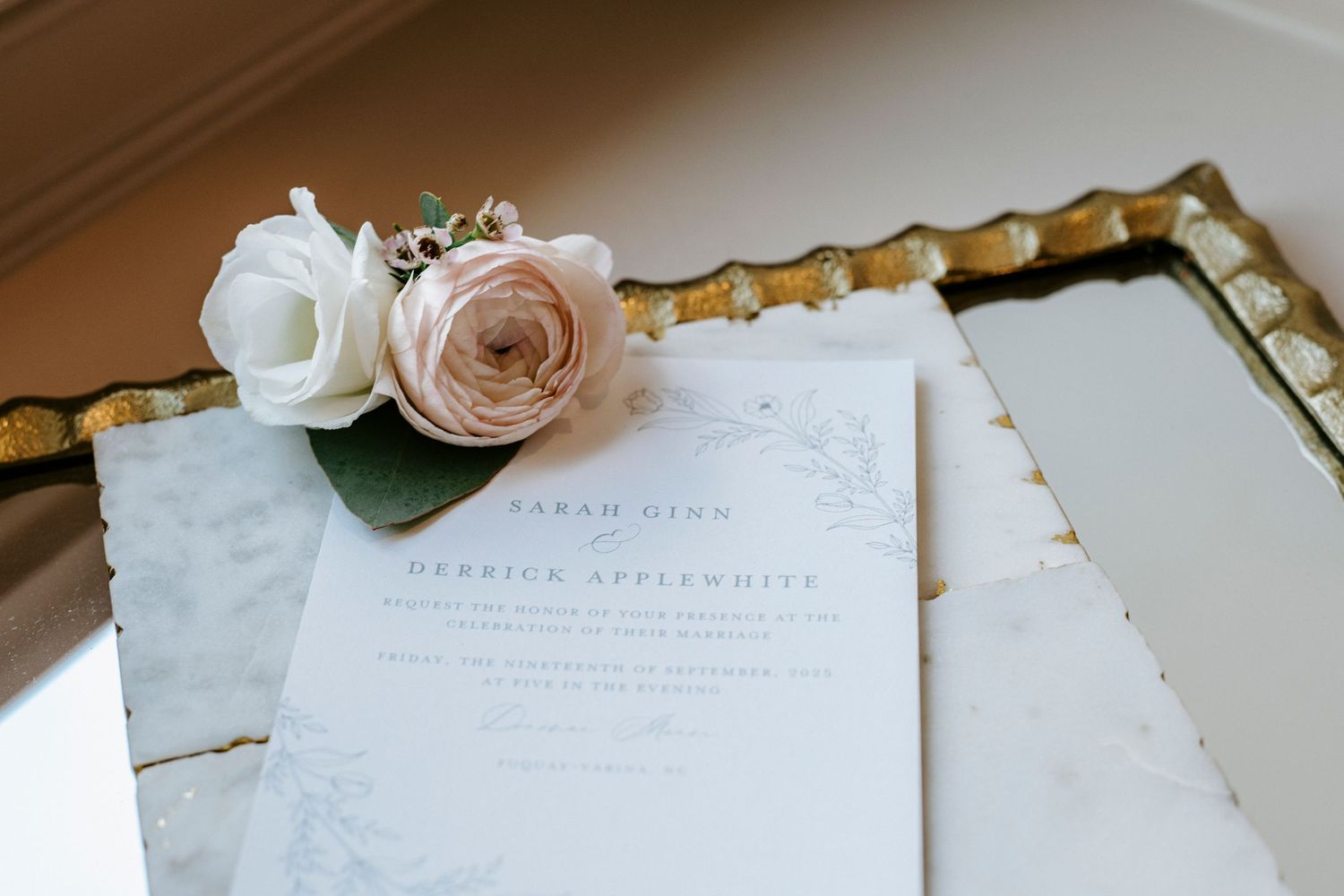 Elegant arrangement of wedding invitation cards and delicate pink roses on white marble surface.