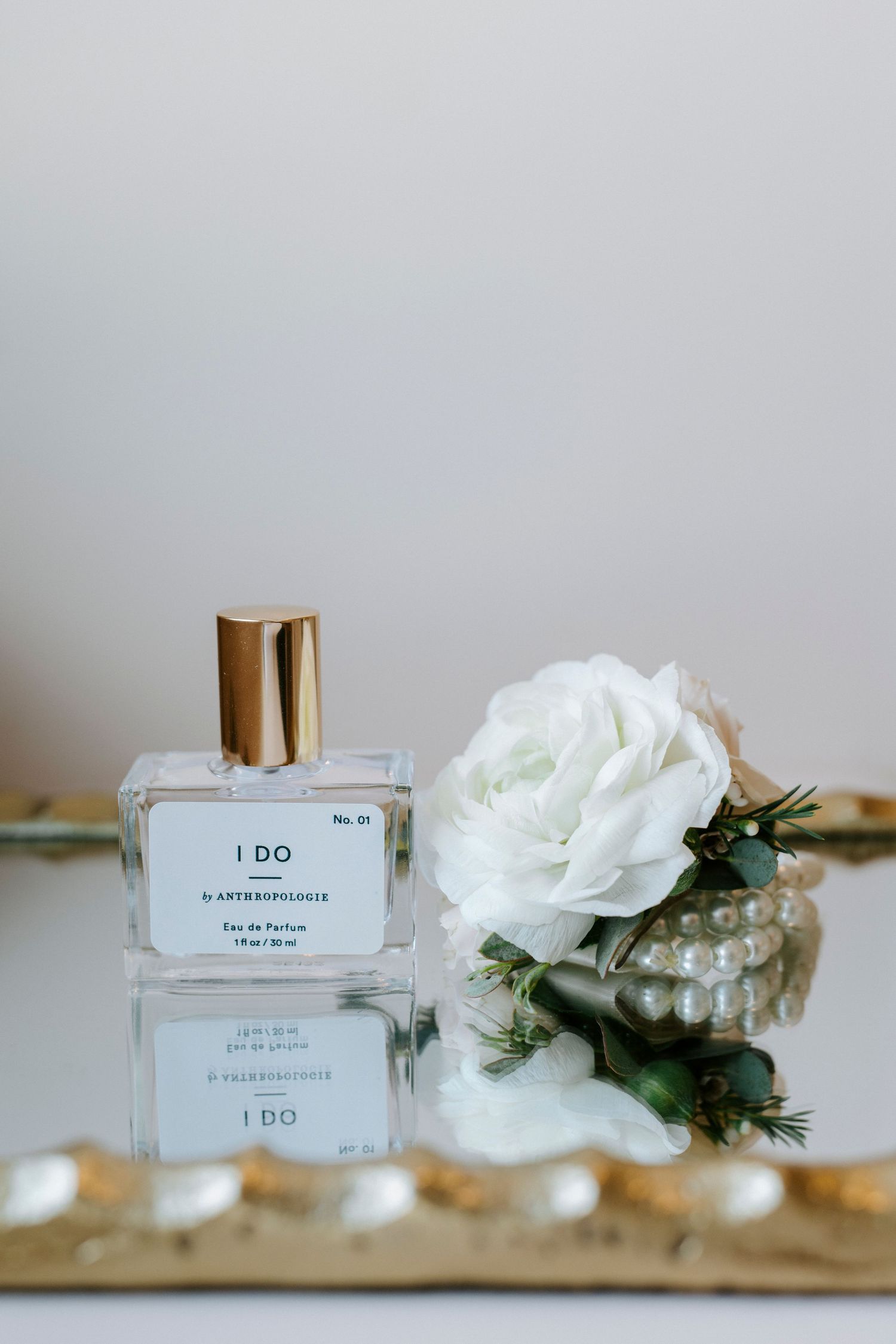 Perfume bottles labeled 'I DO' arranged with white roses and greenery on a wooden surface.