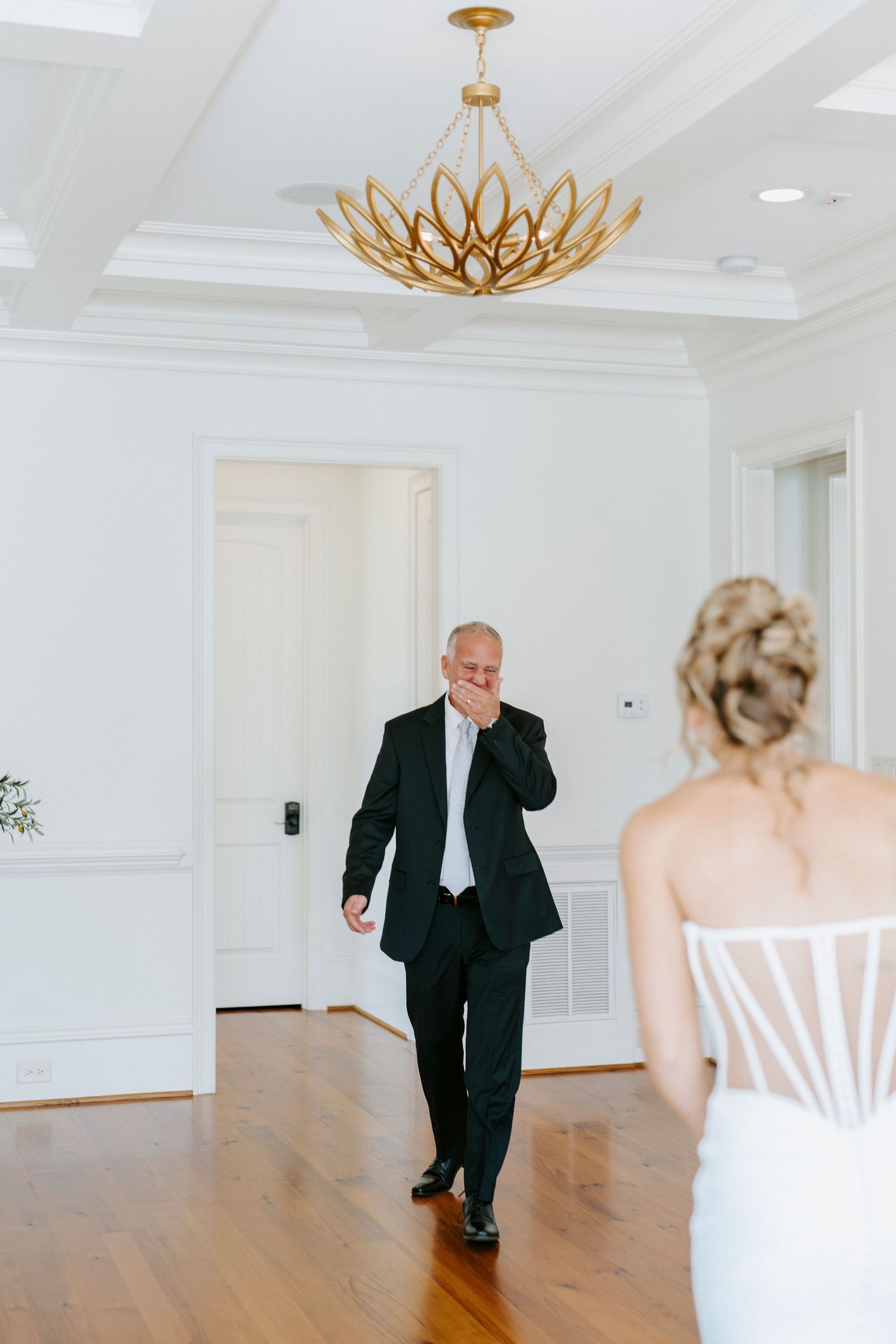An emotional first look moment in an elegant white room with a gold lotus chandelier.