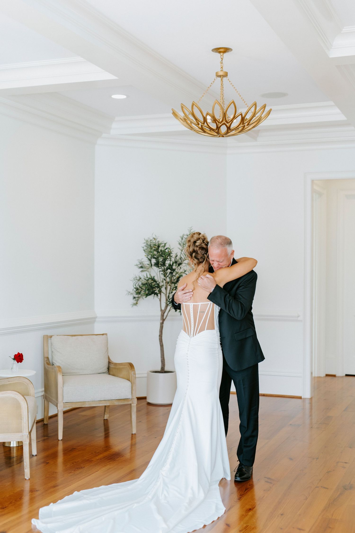 A tender embrace between newlyweds beneath a gold lotus chandelier in a bright white room.