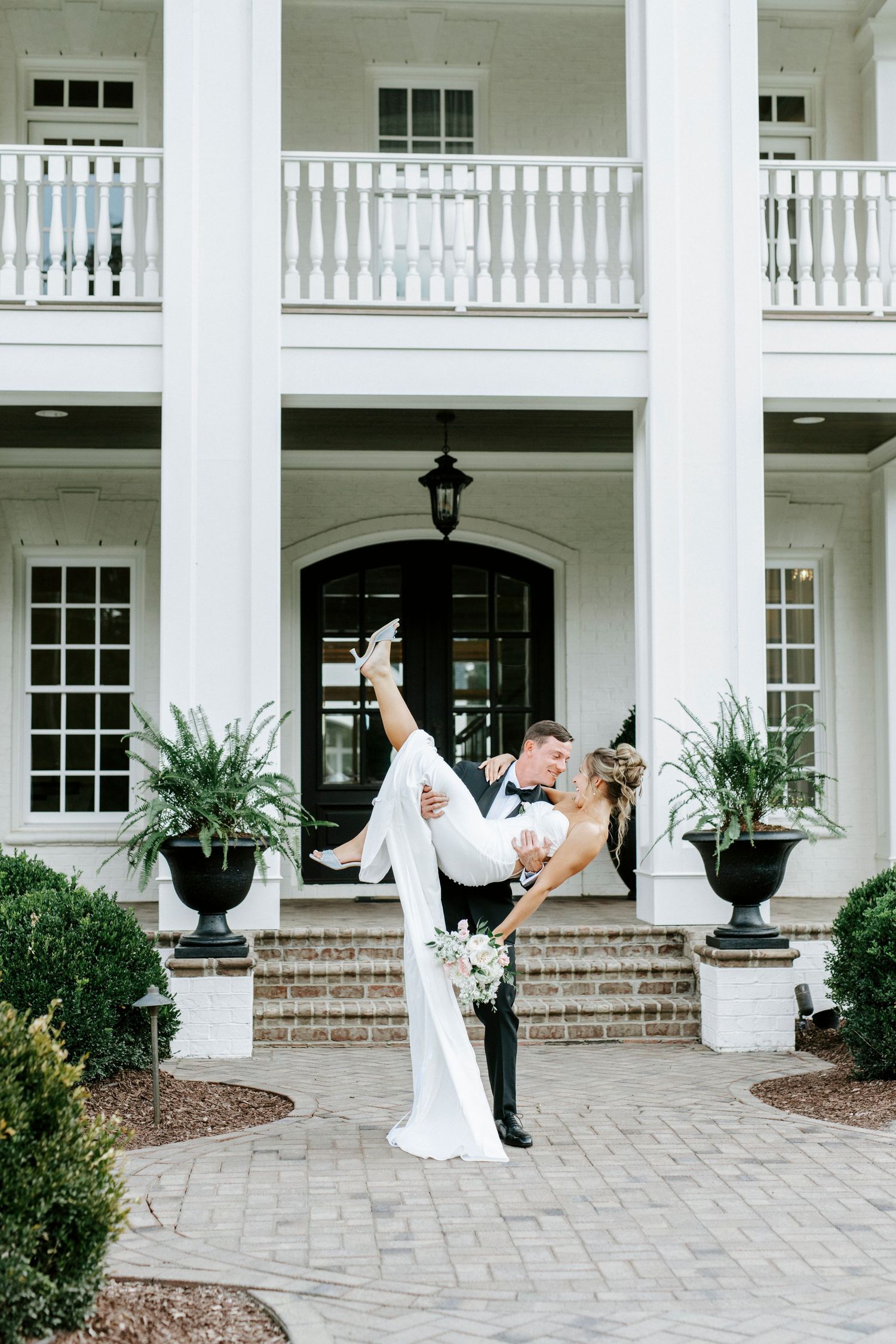A dramatic dip pose by newlyweds on the front steps of a classic white columned mansion.