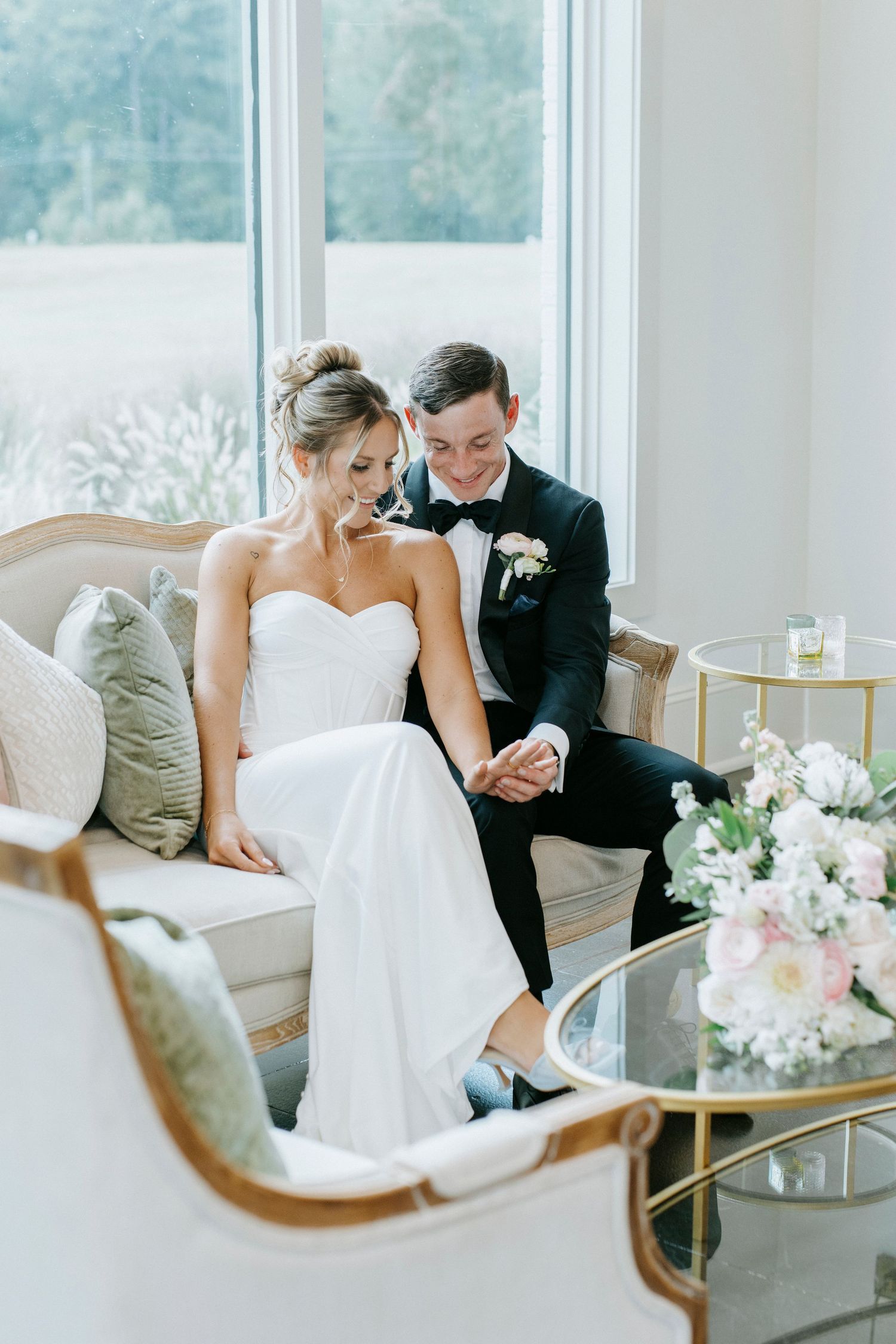 A quiet intimate moment shared on an elegant cream sofa with floral arrangements nearby.