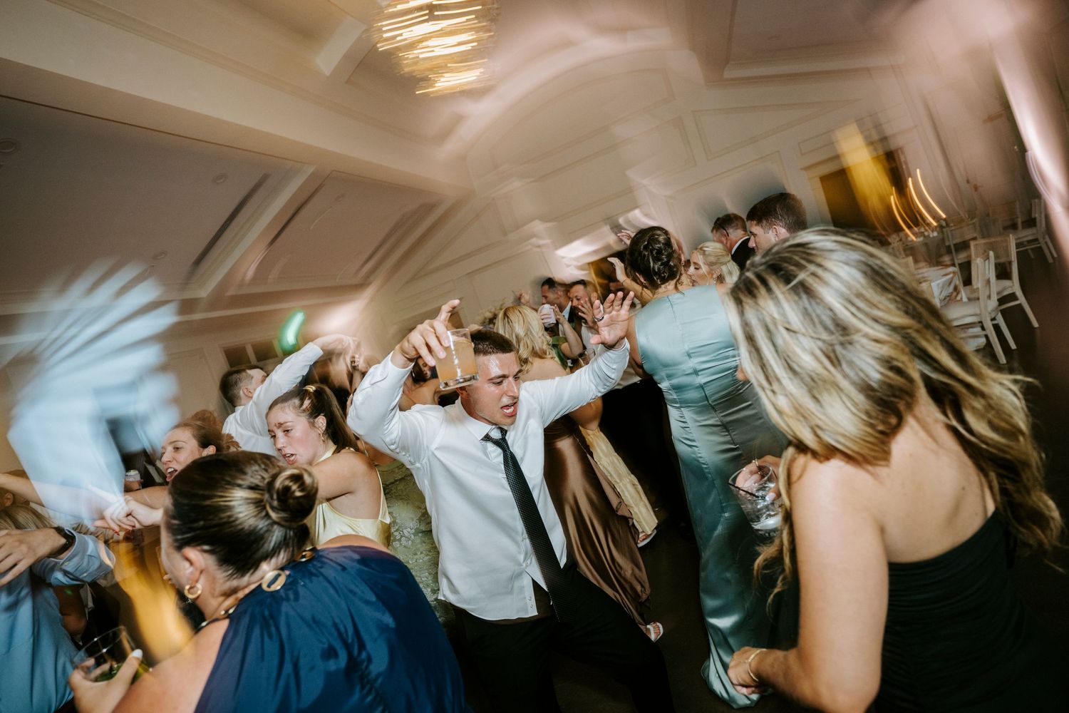 Party guests dancing and celebrating on a dimly lit dance floor during an evening wedding reception celebration.