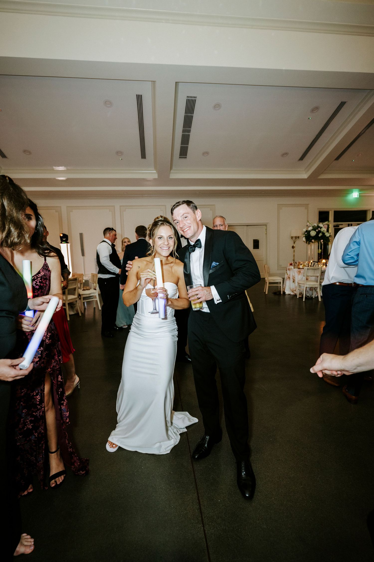 Wedding reception guests dancing and socializing in formal attire at an elegant indoor venue with white decor.