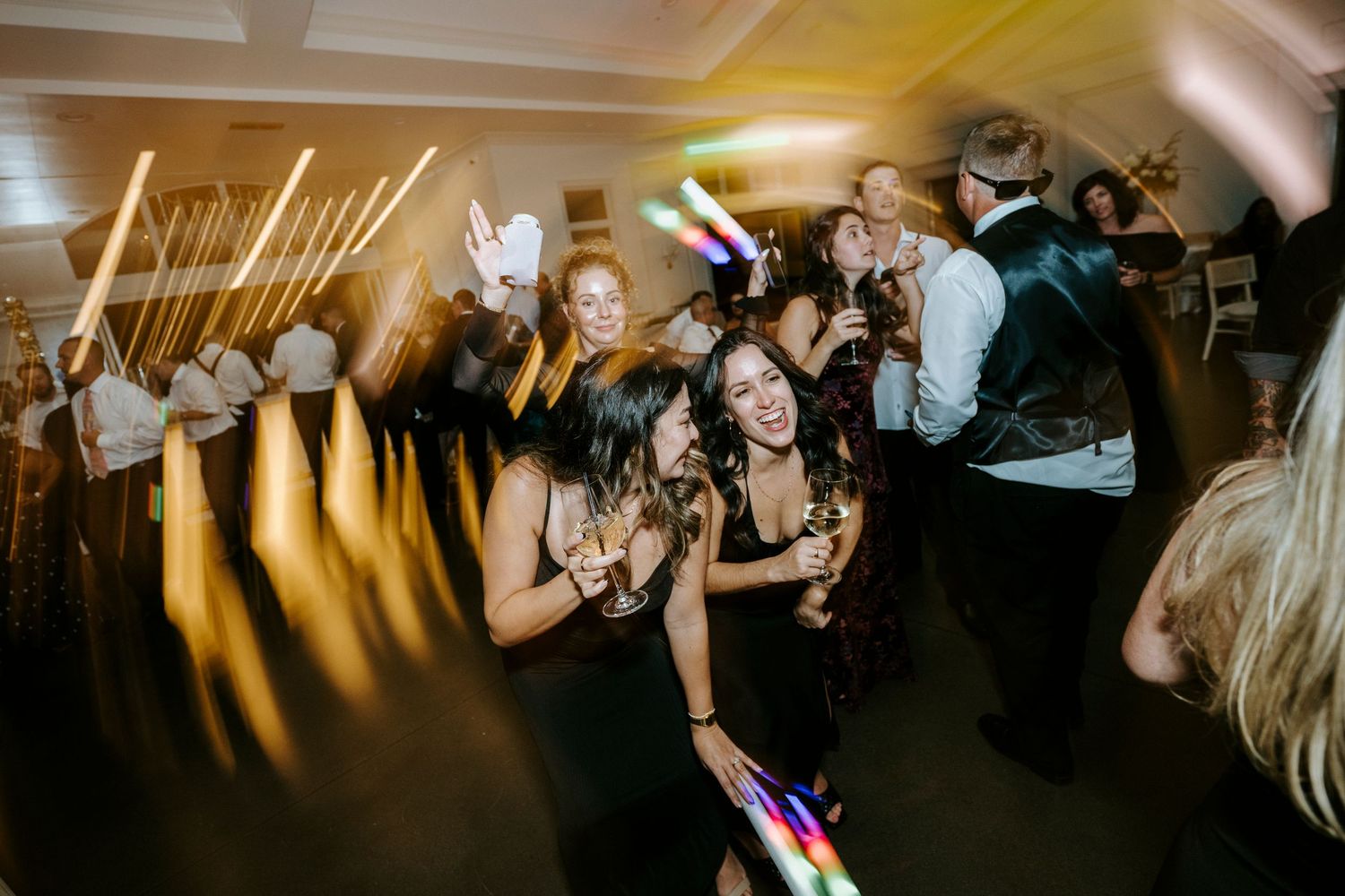 Wedding reception guests dance and celebrate on a crowded ballroom dance floor under warm lighting.