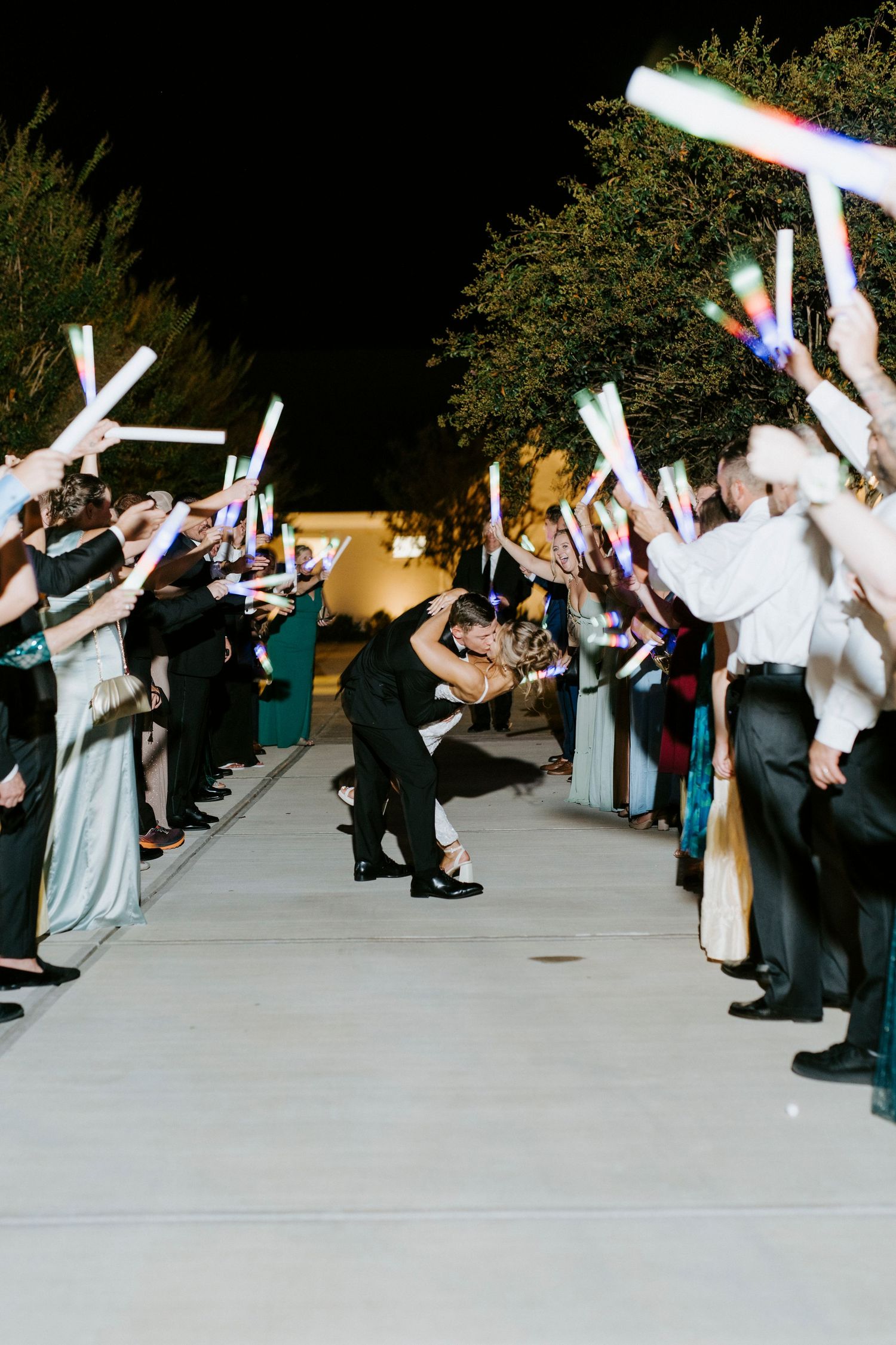 Wedding guests hold glowing LED foam sticks during an outdoor nighttime send-off celebration.