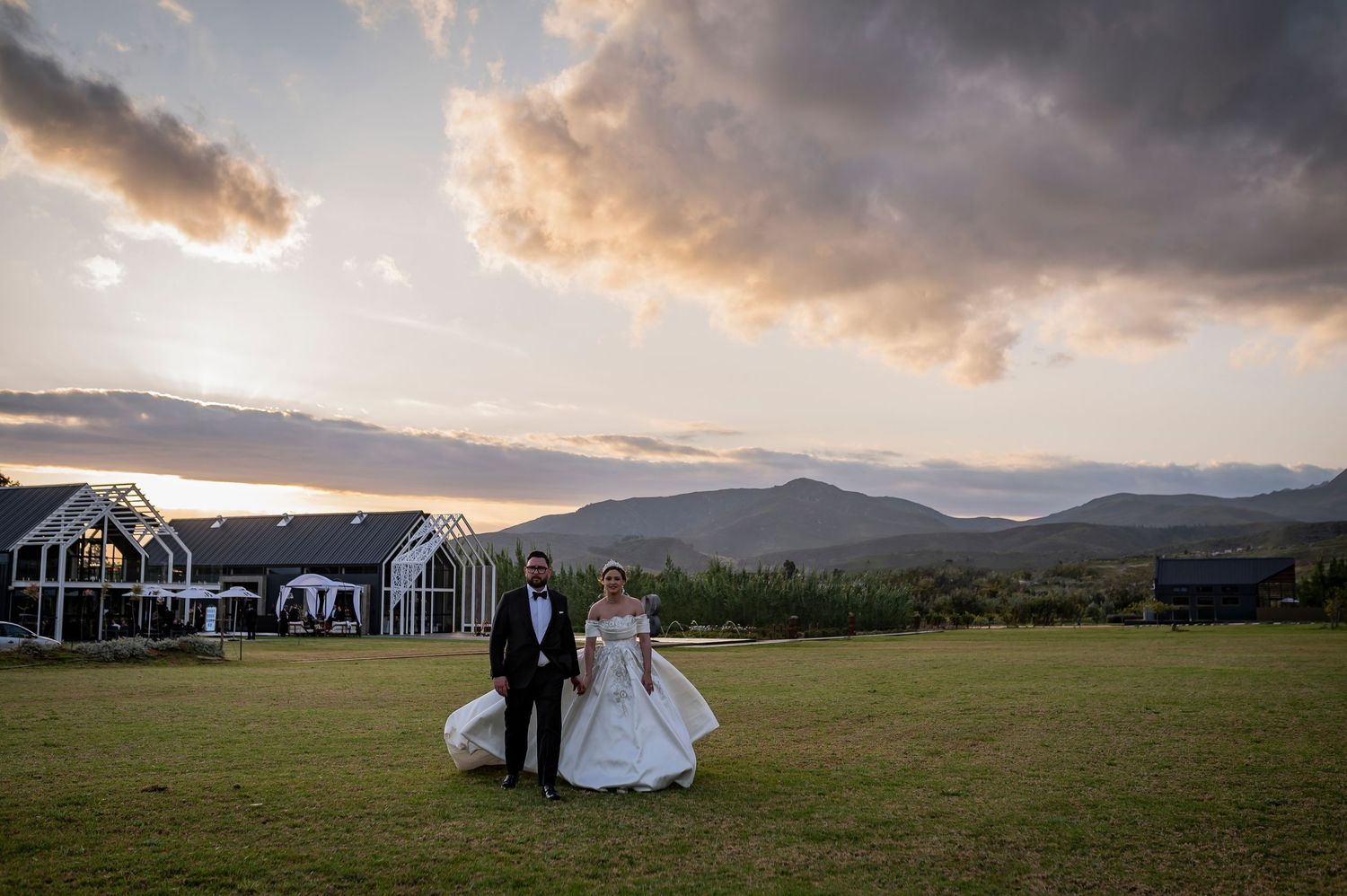 A wedding ceremony takes place on a scenic mountain meadow with dramatic storm clouds at sunset.