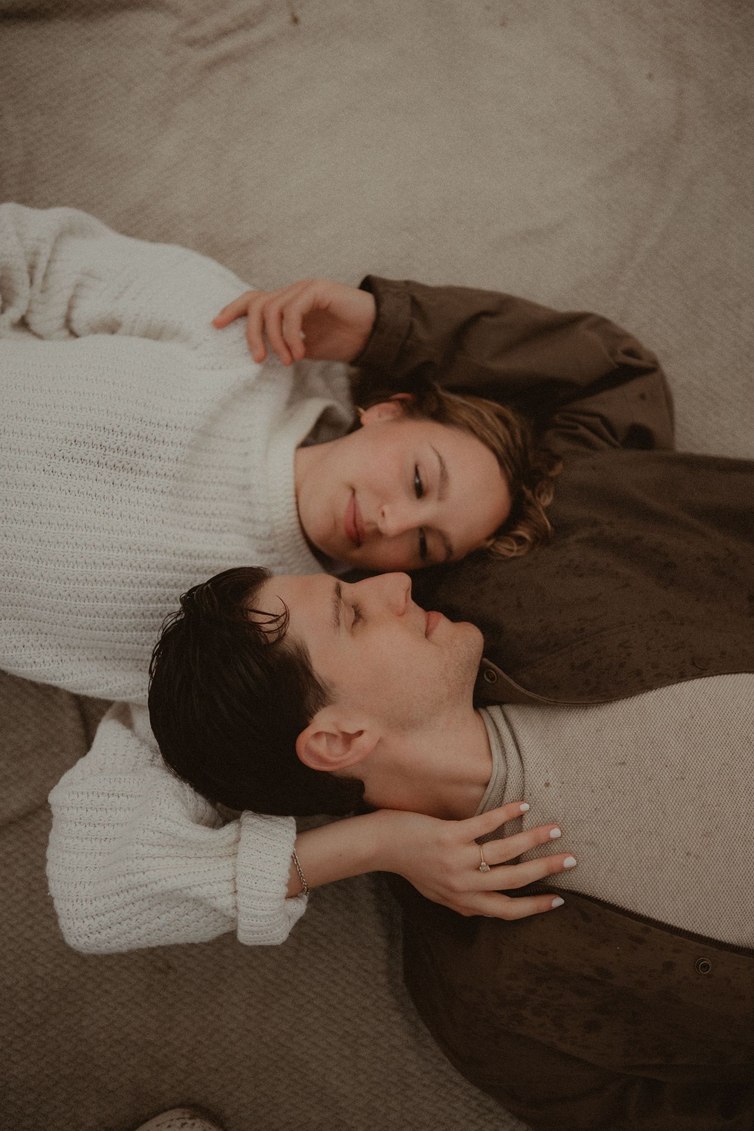 Two people lying on the ground together, wearing cozy sweaters, in an intimate and romantic couple portrait.