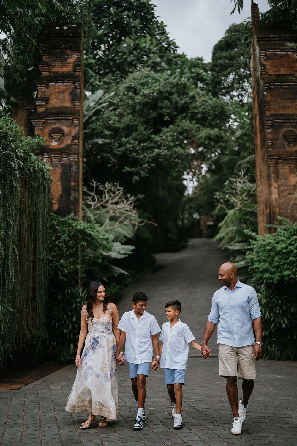 Family walks along stone path surrounded by lush Balinese temple architecture.