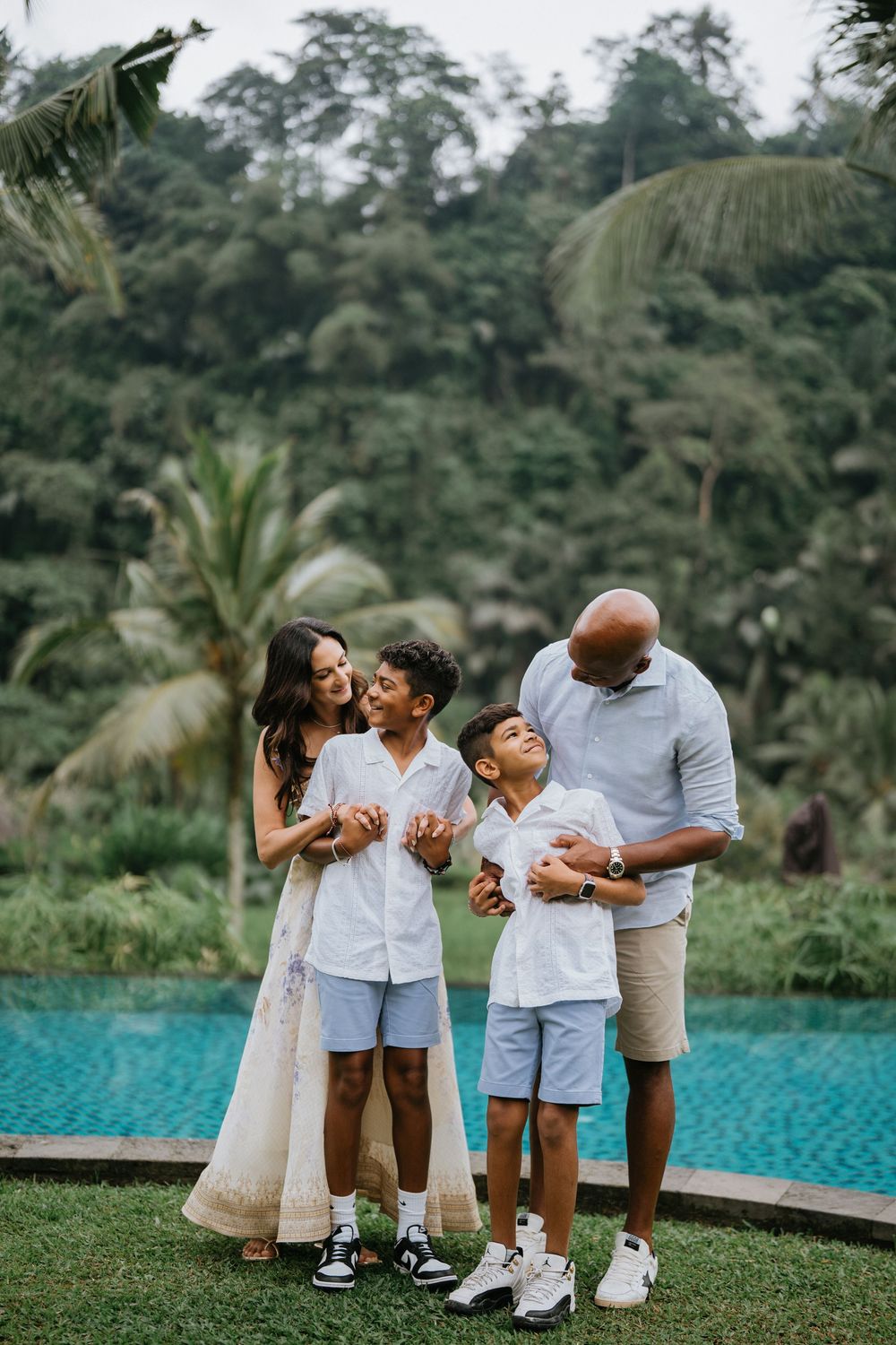 Family in coordinated white outfits poses by tropical infinity pool surrounded by palm trees.