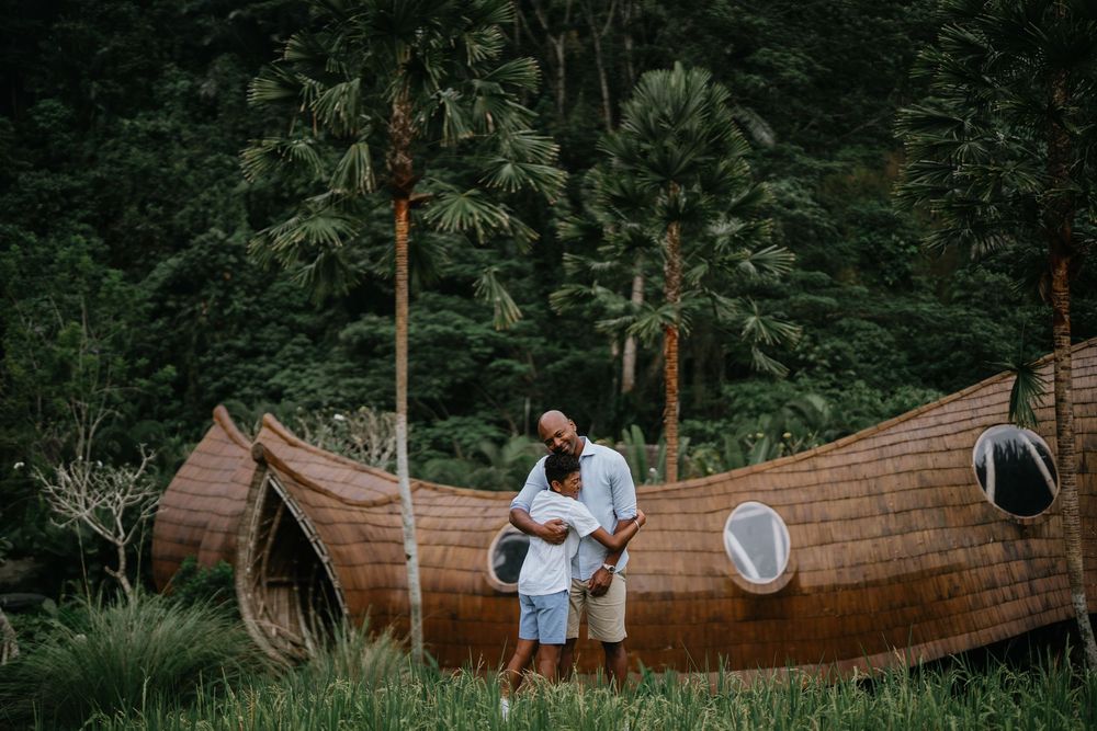 Family members walk together through a tropical garden with traditional wooden structures.