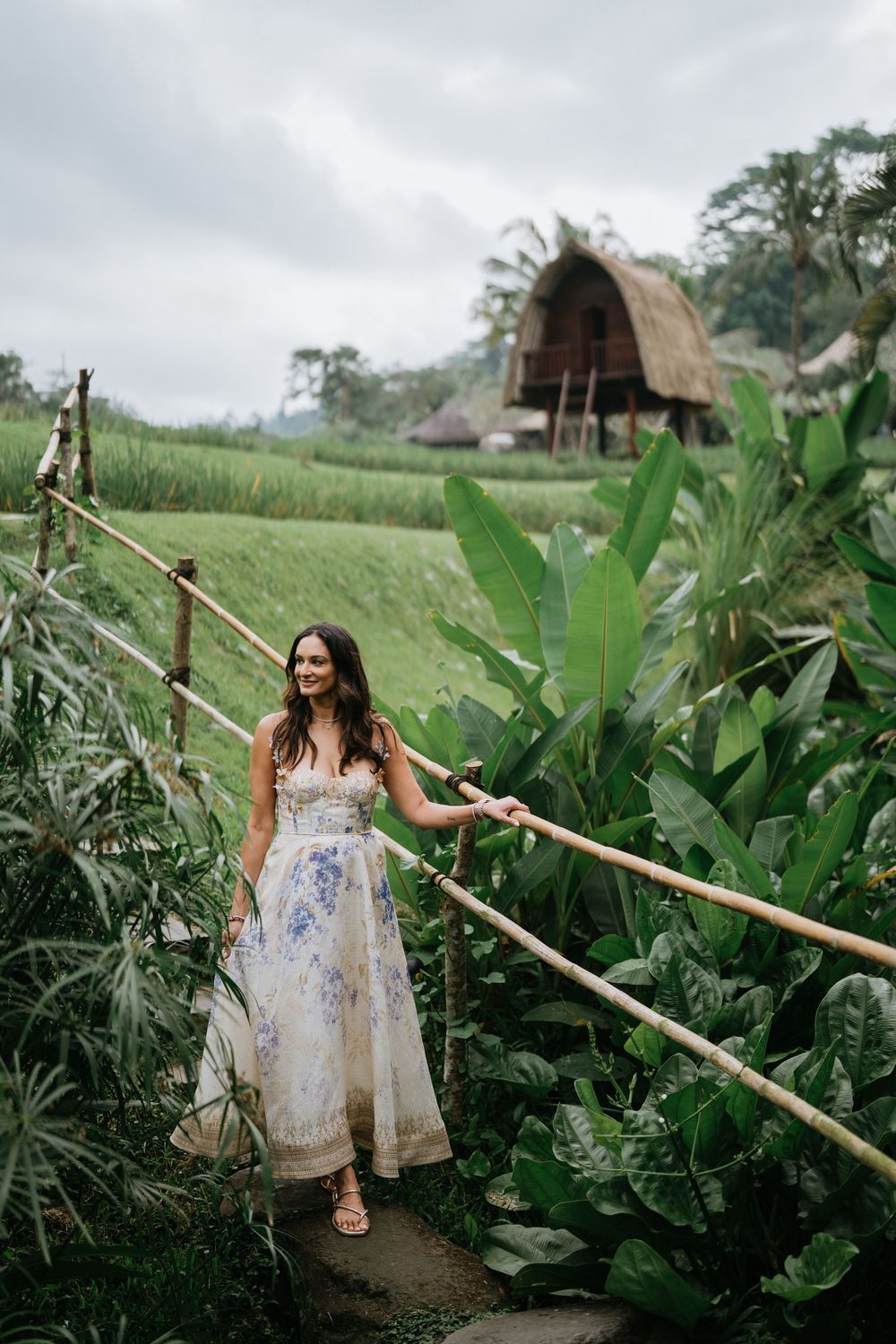 A floral dress catches the breeze along a bamboo pathway surrounded by tropical plants.