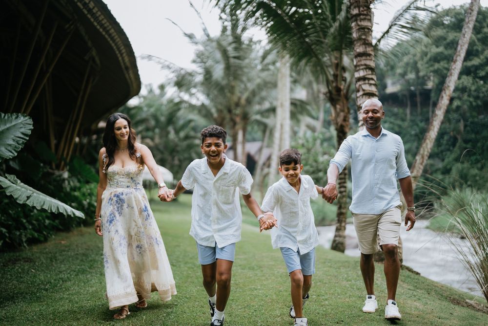 Family members run playfully through a tropical garden setting wearing white outfits.