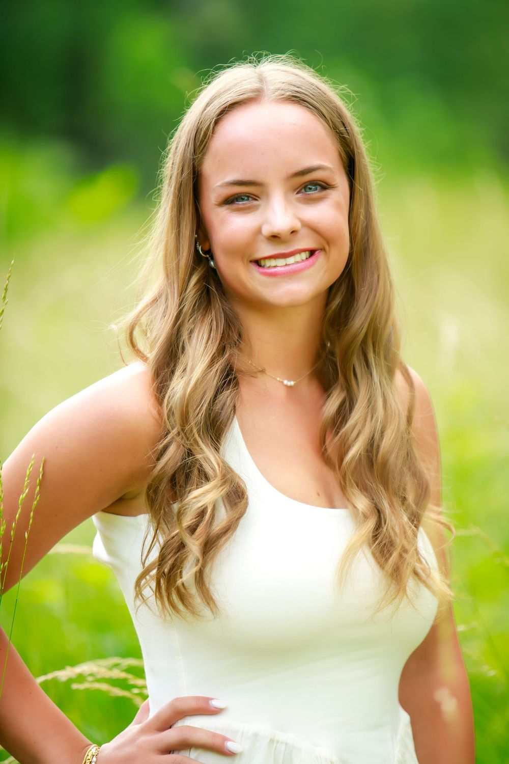 A bright and cheerful outdoor portrait session in a lush green setting with a white sleeveless top.