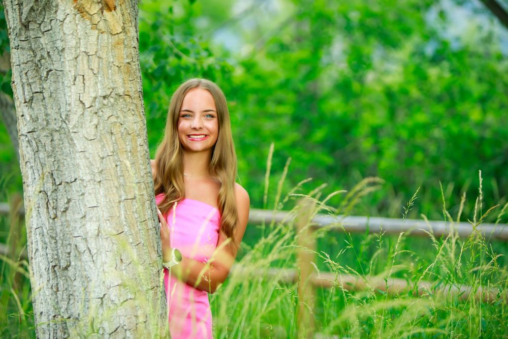 Person sits by a tree in a lush green field wearing a bright pink top on a sunny summer day.