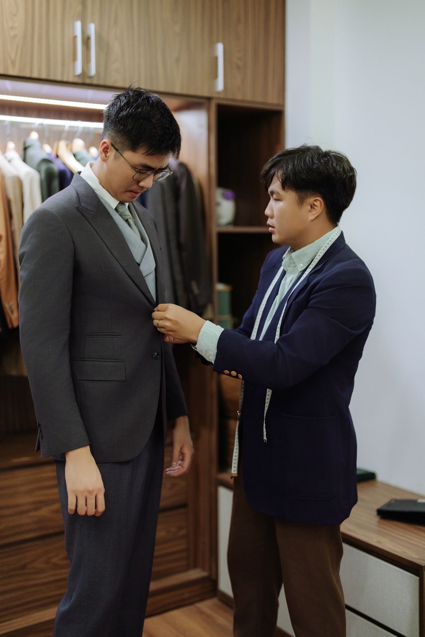 Tailor fitting a gray suit jacket on a client inside a professional menswear boutique.
