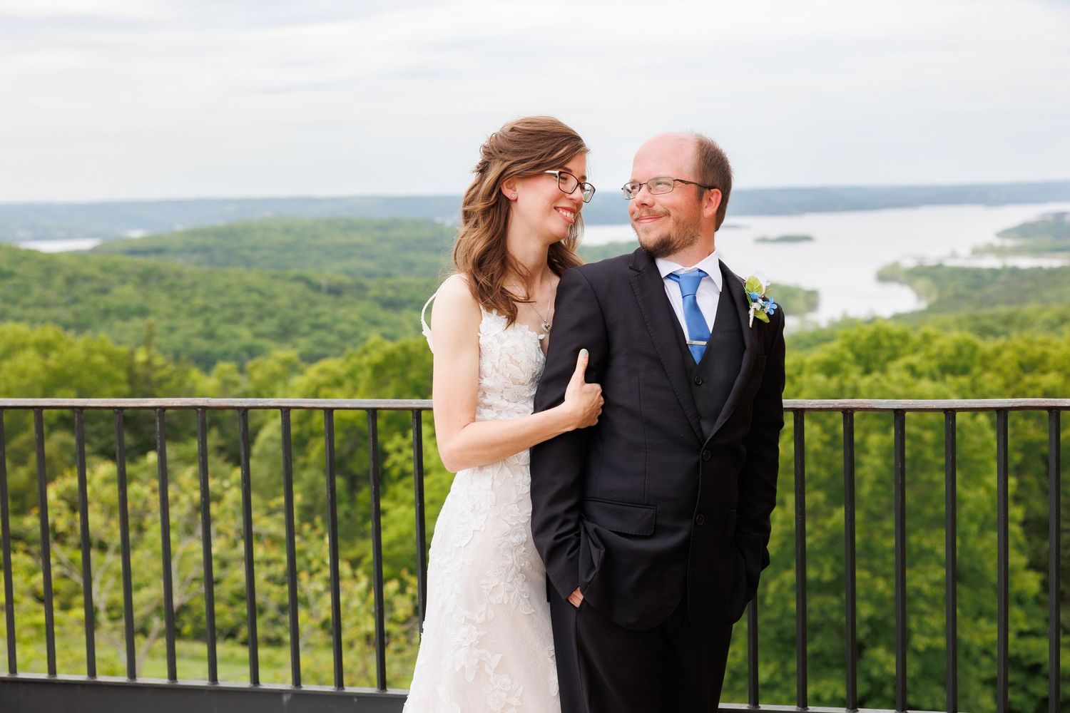 A wedding couple shares an intimate moment overlooking a scenic green landscape from a hilltop balcony at Top of the Rock.