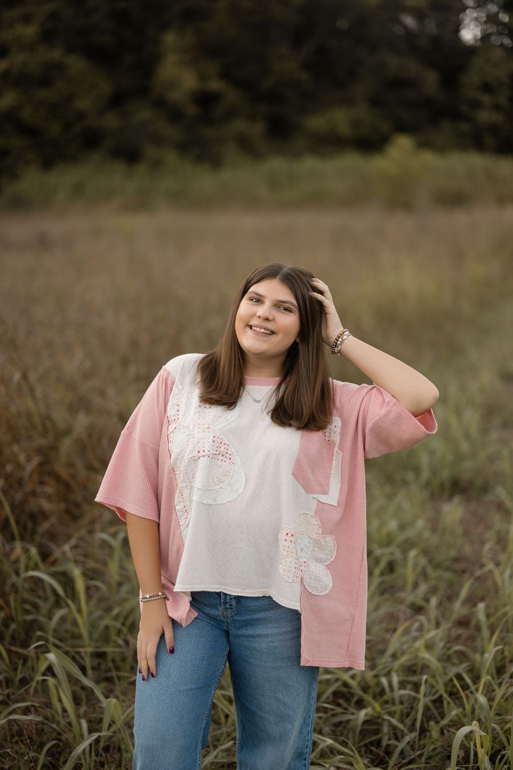 Person stands in tall grass wearing casual pink and blue outfit during outdoor photo session.