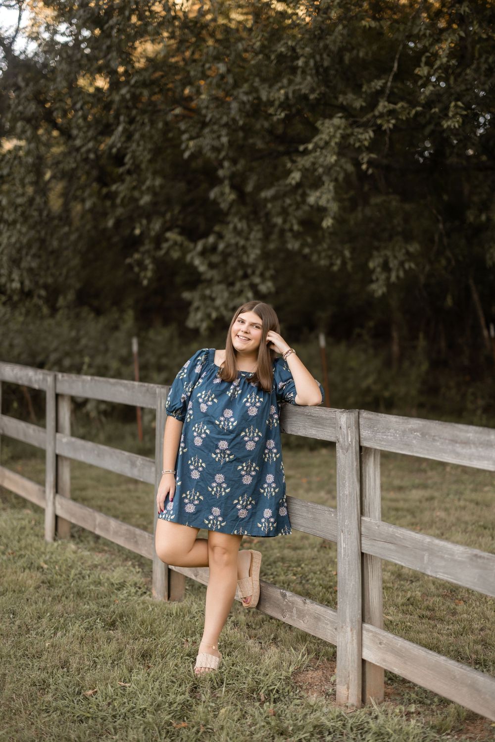 A floral print navy blue dress is worn in a casual outdoor setting with a wooden fence and trees in the background.