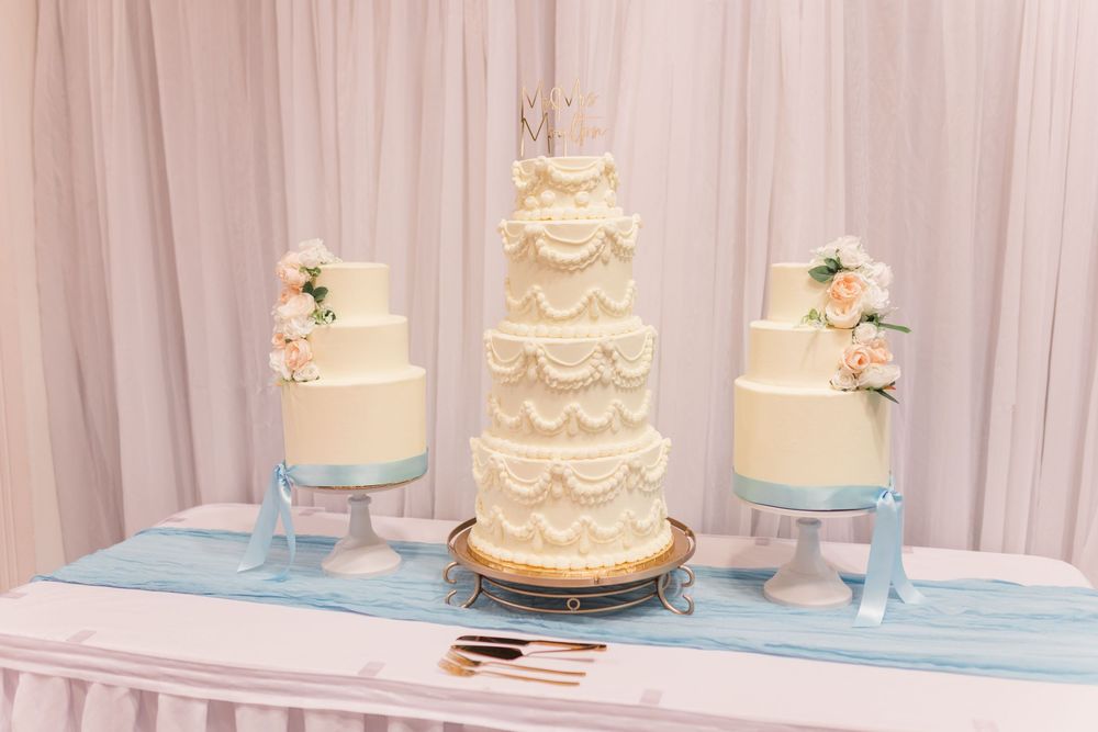 Elegant ivory wedding cake display with pale blue accents and delicate white floral decorations.