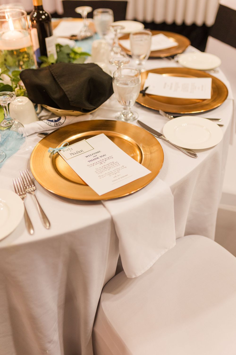 Elegant place settings with gold charger plates, white tablecloths, and black napkins at a formal dining event.