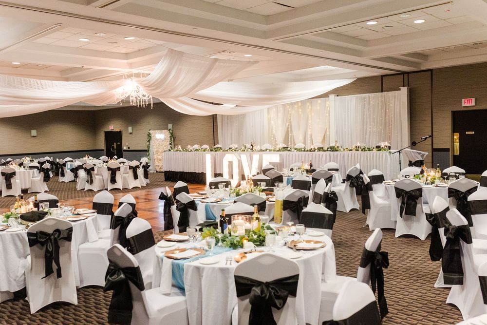 Elegant wedding reception venue with black and white chair covers and yellow floral centerpieces illuminated by warm lighting.