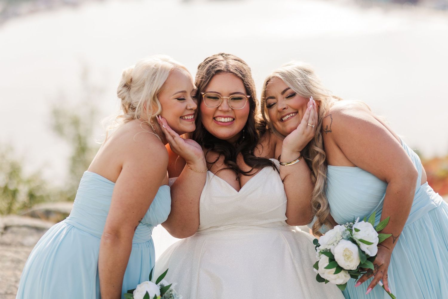 A group of bridesmaids in light blue dresses embrace the bride in a joyful moment during a wedding photoshoot.