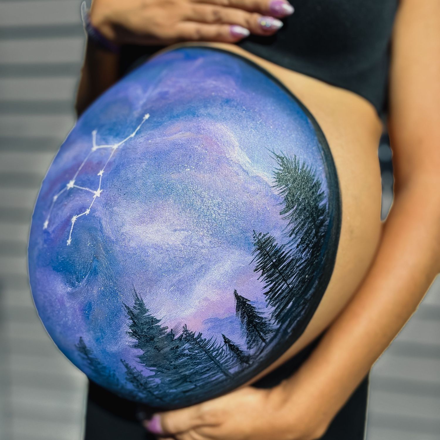 Hand-painted maternity belly art showing nighttime forest scene with stars and galaxies.